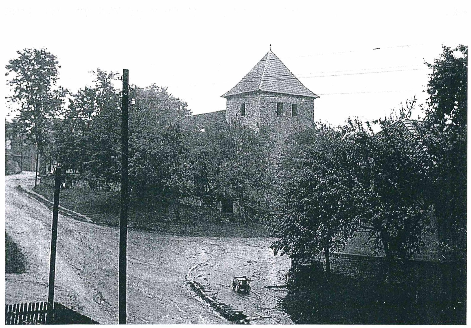 Historisches Foto der Lange Straße mit Holzmasten und Kirchturm, davor ein Leiterwagen mit Milchkanne