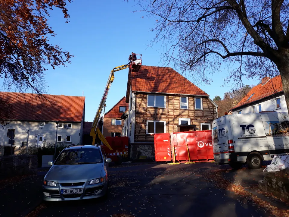 Das Haus Lange Straße 27 mit abgenommenem Behang: unter der Verkleidung kommt das Fachwerk zum Vorschein, ein Hubsteiger steht am Giebel, davor Container und ein Transporter.