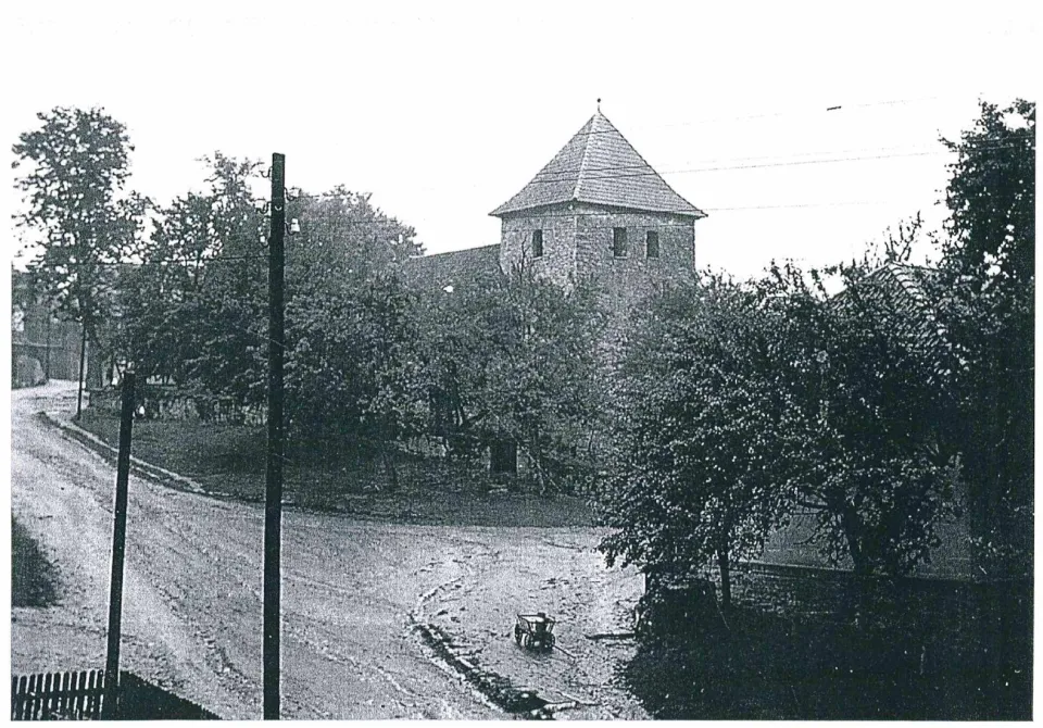 Historisches Foto der Lange Straße mit Holzmasten und Kirchturm, davor ein Leiterwagen mit Milchkanne